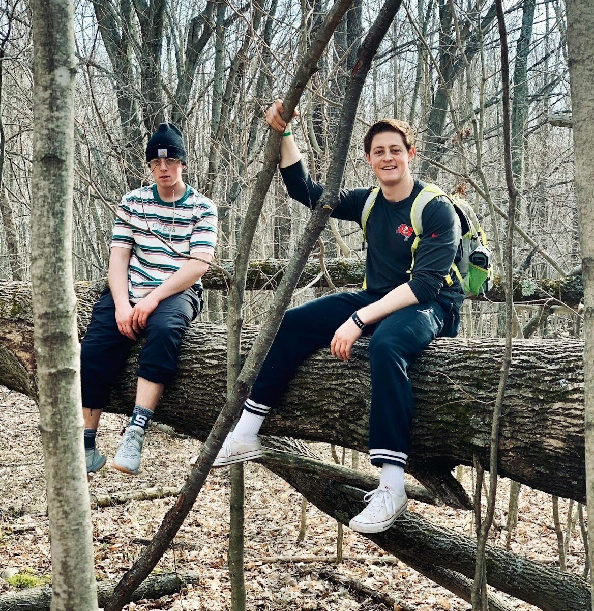two young men sitting on a fallen tree in the woods